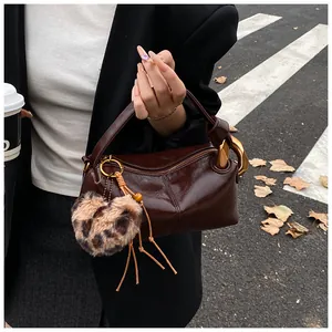 Close-up of deep brown glossy leather boston bag with leopard heart charm and gold hardware
