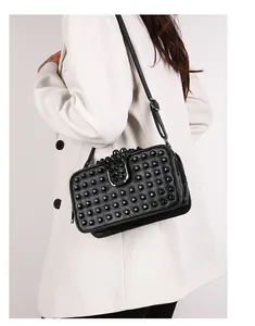Detail view of black studded crossbody bag with metallic buckle on white blazer