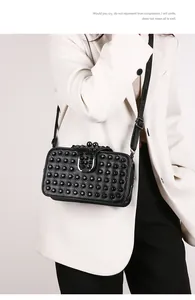 Detail of black studded leather crossbody bag with metallic clasp on a white blazer