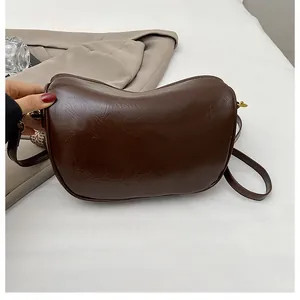 Detail of dark brown crescent bag with soft pleats and glossy faux leather texture