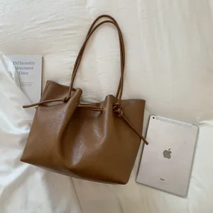 Retro brown leather tote bag with drawstring closure on a soft white fabric background