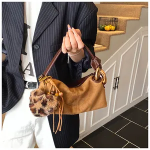 Detail of vintage brown suede pillow bag with oversized gold chain and leopard pom-pom