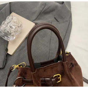 Detalle de bolso tipo cubo marrón oscuro mate con herrajes dorados y asa de cuero