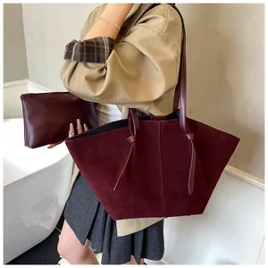 Gros plan sur l'ensemble sac fourre-tout et pochette en daim bordeaux porté par un mannequin
