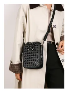 Detail view of a black studded crossbody bag with silver U-shaped metal ring on a beige coat