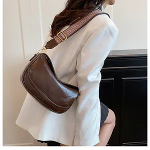 Detail of deep brown crescent bag with pleated leather texture and woven strap