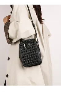Detail of black leather crossbody bag with hemispherical studs on trench coat