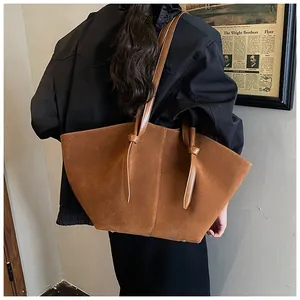 Détail d'un grand cabas en daim marron avec lanières nouées porté par un mannequin
