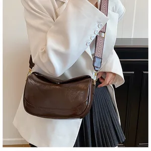 Detail of dark brown crescent bag with glossy leather texture and jacquard strap