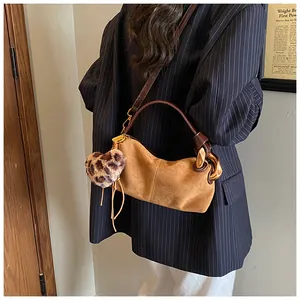 Detail of suede crescent bag with leopard heart charm and gold hardware on shoulder