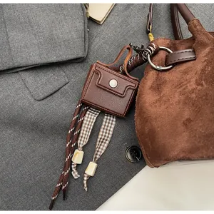 Detalle de un mini colgante de bolso marrón con cuerda trenzada y lazo de cuadros