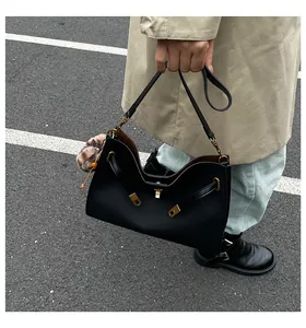 Detalle de bolso de cuero negro con corte en V, hebilla dorada y colgante de pompón suave