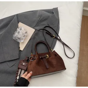 Detalle de bolso cubo marrón oscuro mate con hebilla de correa y adorno de cinta a cuadros