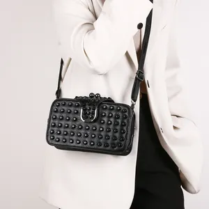 Fashionable black studded crossbody bag with silver buckle worn on a white suit jacket