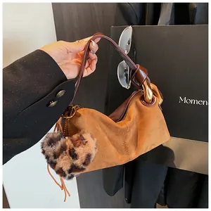 Detail of a brown suede handbag with a large gold chain handle and leopard pompom