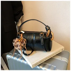 Detail of black glossy cylindrical handbag with gold hardware and heart leopard charm