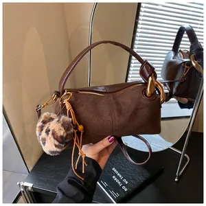 Detail of dark brown suede handbag featuring leopard pom-pom and metallic ring handle