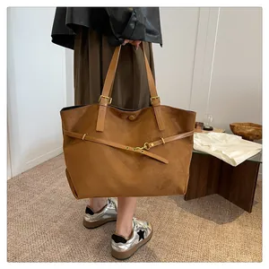 Close-up of brown suede tote bag featuring premium leather straps and vintage metal buckles