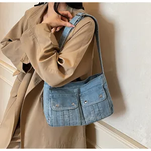 Detail of blue denim shoulder bag featuring front pockets and decorative stitching