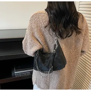 Dettaglio borsa hobo nera opaca con catena argentata su maglione lavorato