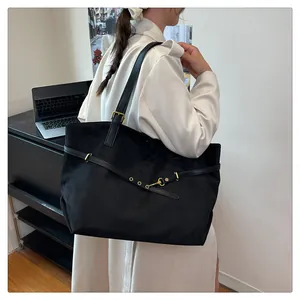 Detail of black suede tote bag with gold buckle on a model wearing white trench coat
