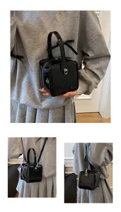 Detail of glossy black patent leather box bag with embossed logo and silver metallic buckle