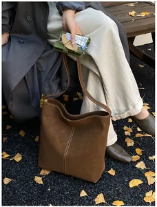 Detail der braunen Wildleder-Beuteltasche mit Kontrastnaht vor Herbstlaub und grauem Mantel