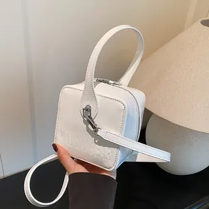 Detail of white patent leather box bag featuring embossed logo and metal zipper
