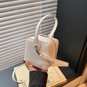 Close-up of white glossy box bag with top handle and MAUDAI BEAR embossed lettering