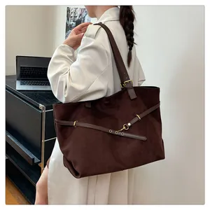 Model wearing dark brown suede tote bag in office setting with long shoulder strap