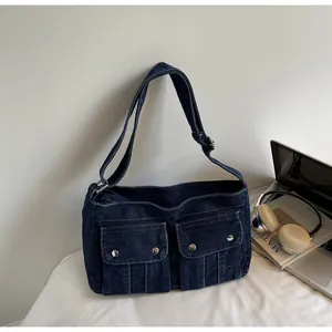 Detail of blue denim crossbody bag with dual pockets on a desk with a laptop