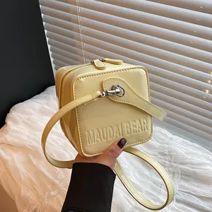 Detail of light yellow patent leather square bag with embossed text and silver buckles