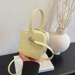 Detailed view of yellow glossy square box bag with embossed MAUDAI BEAR logo texture