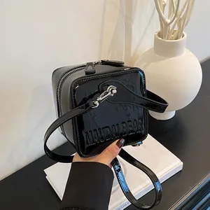 Detail of black patent leather square box bag with embossed logo and silver hardware