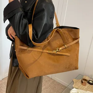 Brown suede tote bag with leather straps and metal buckle shown on a model