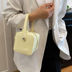Detail view of cream square box bag featuring embossed logo and premium patent leather