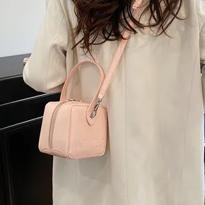Pink patent leather cube bag with silver zipper and logo detail on a white blazer