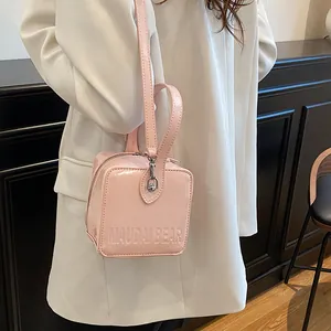 Detail of pink patent leather box bag featuring embossed logo and metallic finish