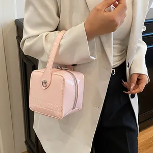 Detail of pink glossy patent leather box bag featuring top handle and embossed logo