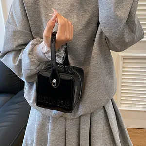 Detail of black glossy patent leather box bag with embossed logo and metal lock