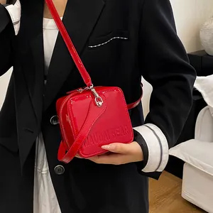Close-up of bright red glossy box bag worn with a black suit for a stylish contrast