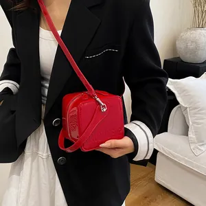 Close-up of a vibrant red patent leather square box bag with embossed logo detail