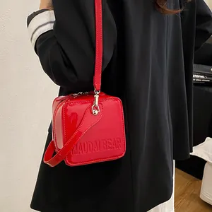 Detail of red patent leather crossbody box bag with embossed logo worn over a dark blazer