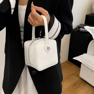 Detail view of a white box bag with a top handle, metallic clasp, and embossed text