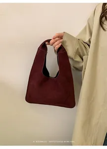 Primer plano de un bolso tote de gamuza burdeos llevado por modelo con gabardina beige
