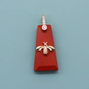 Macro shot of red trapezoid natural stone pendant with gold bee relief and crystal bail