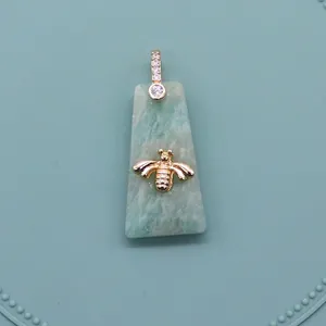 Macro detail of trapezoid natural stone pendant with gold bee motif and zircon clasp