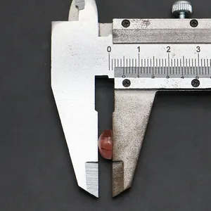 Primo piano di una pietra di agata rossa da 7 mm misurata con un calibro per gioielli fai-da-te