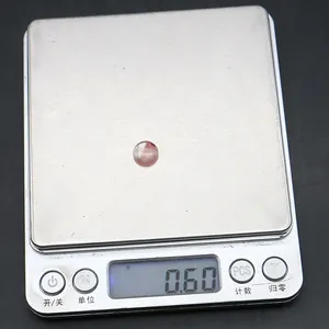 Bilancia digitale che mostra il peso di 0,60g di una pietra tonda occhio di tigre rossa
