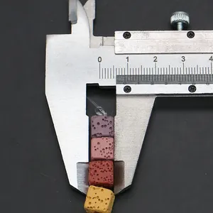 Macro shot of 8mm square lava stone beads in purple and pink being measured with a caliper